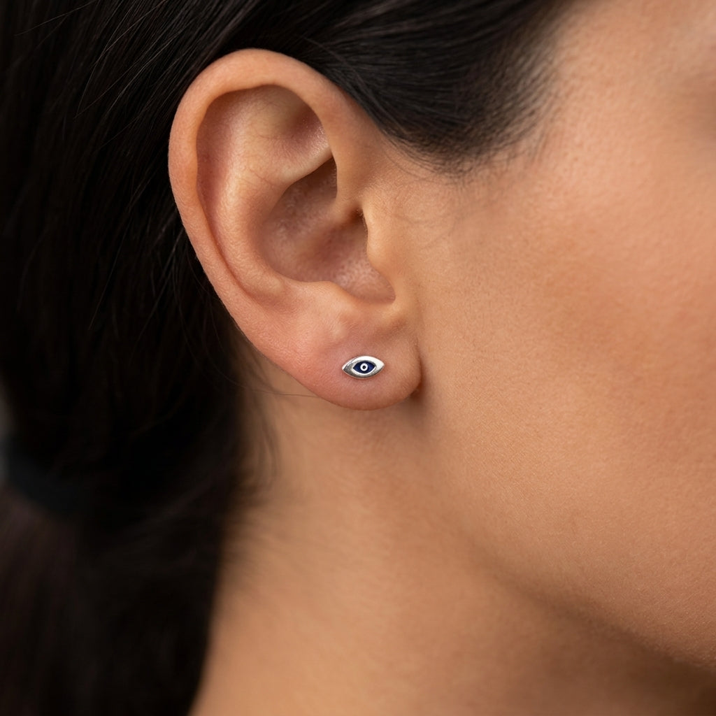 A close-up of a person's ear wearing a small silver stud earring with a white and dark blue evil eye design.