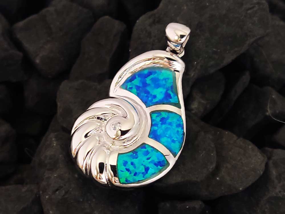 A silver pendant in the shape of a Nautilus seashell made of silver and blue opal stones on black rocky background.