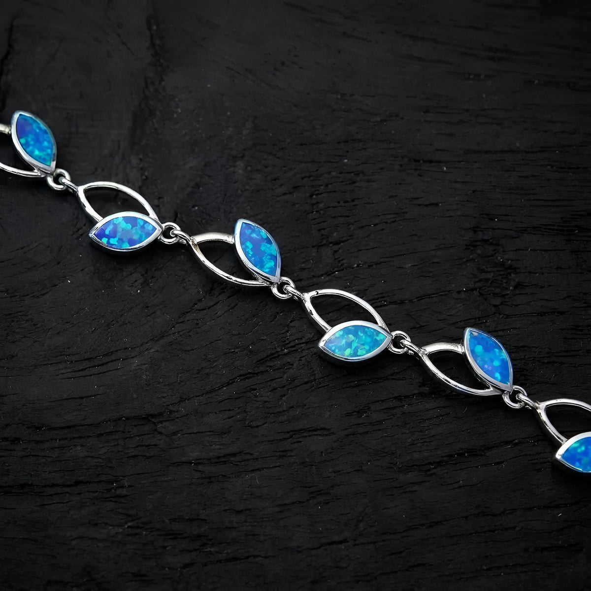 A silver link bracelet featuring marquise-cut blue opal gemstones, displayed diagonally on a dark textured background.
