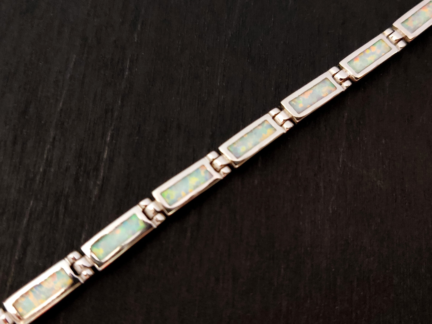 Silver bracelet made of white opal stones on black background.