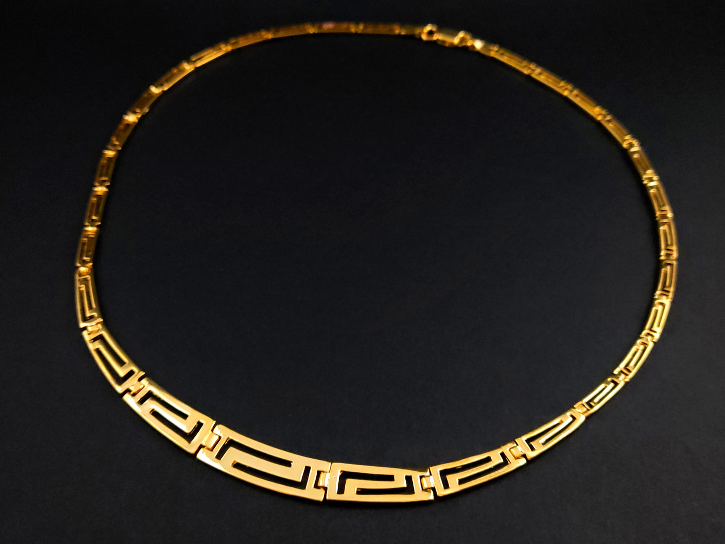 Greek Key silver necklace with gold plated finish in a gradual pattern on black background.
