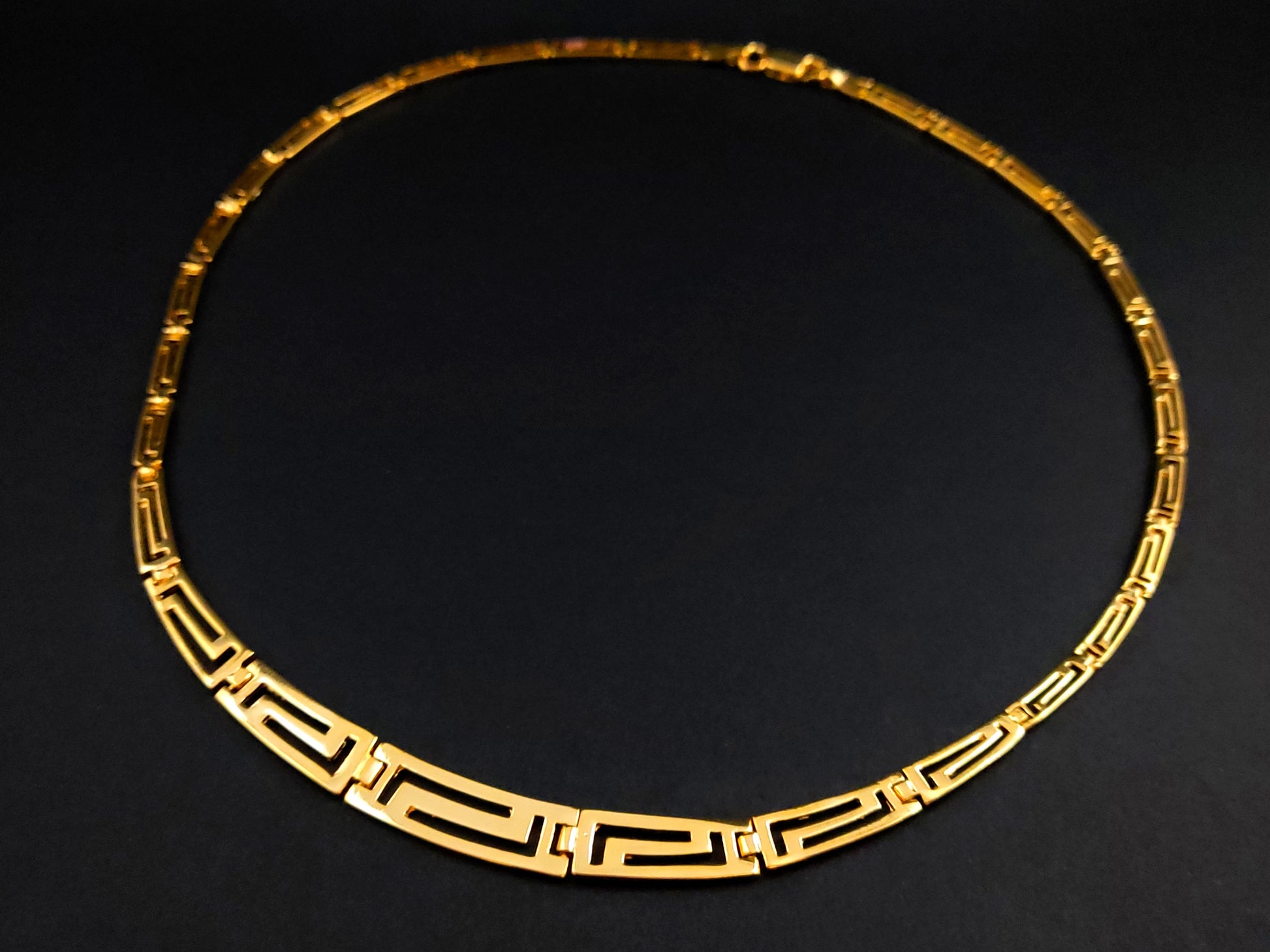 Greek Key silver necklace with gold plated finish in a gradual pattern on black background.