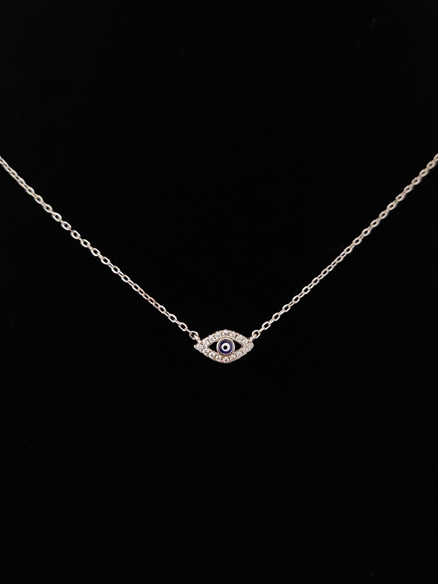 Silver evil eye fine necklace with black background.