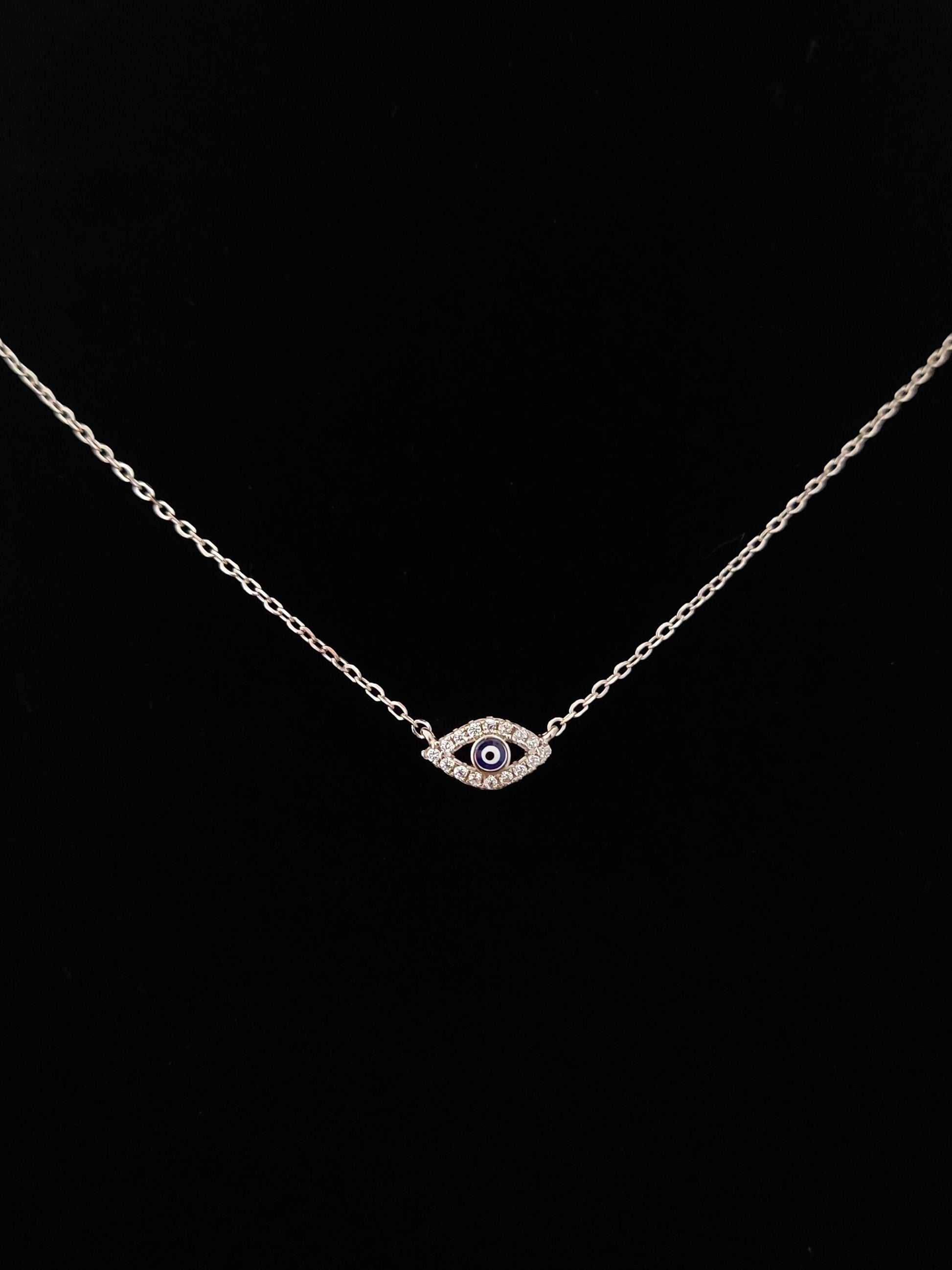 Silver evil eye fine necklace with black background.