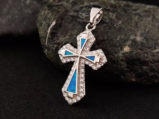 A sterling silver 925 cross made with blue opal stones and white crystals on black background.
