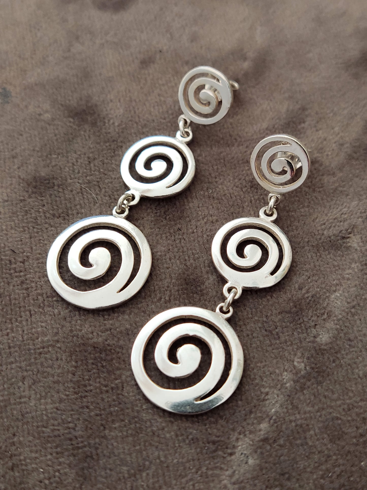 Greek silver dangle earrings with a triple spiral design on gray velvet.