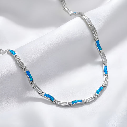 Greek Key silver necklace with blue stones on a white fabric background