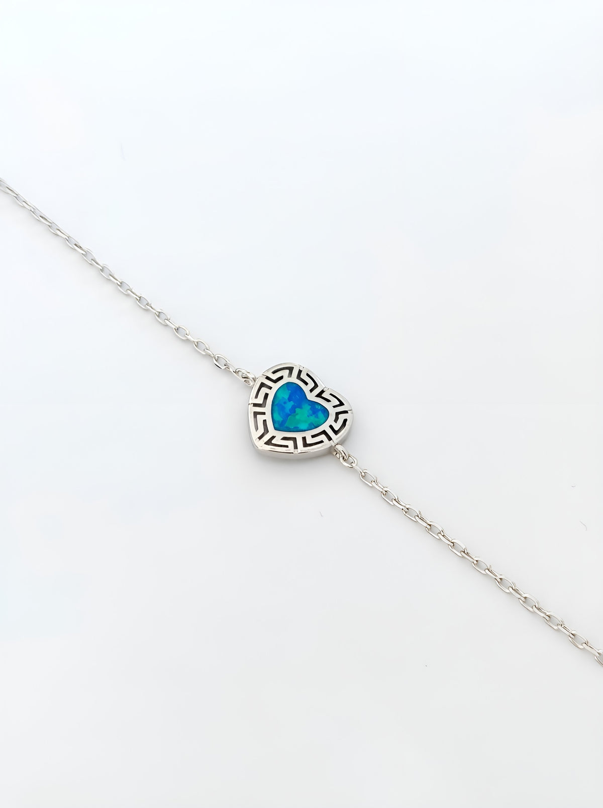 A delicate silver chain bracelet featuring a small heart-shaped opal pendant with a black Greek key border, displayed on a clean white background.