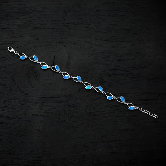 A silver link bracelet featuring a series of marquise-cut blue opal stones, displayed diagonally on a dark textured wooden surface.