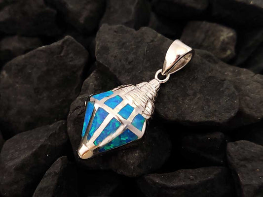 A silver pendant in the shape of an oyster with blue opal stones lying on black rocky background.