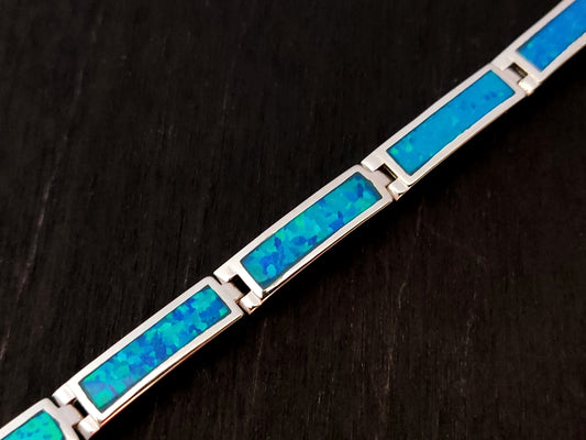 Silver bracelet with blue opal stones on black background.