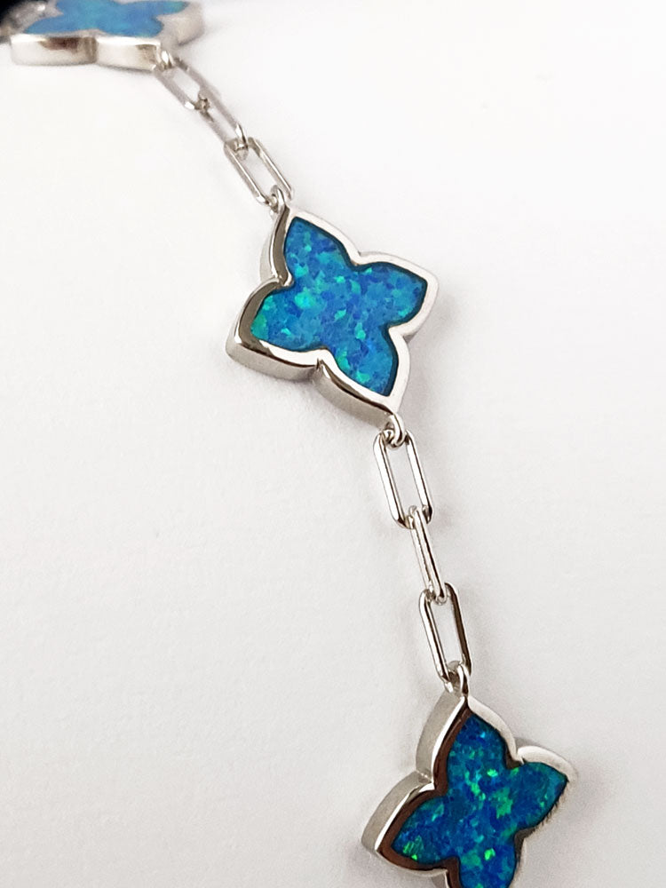 Close-up photo of a silver bracelet with blue opal stones in cross shape.