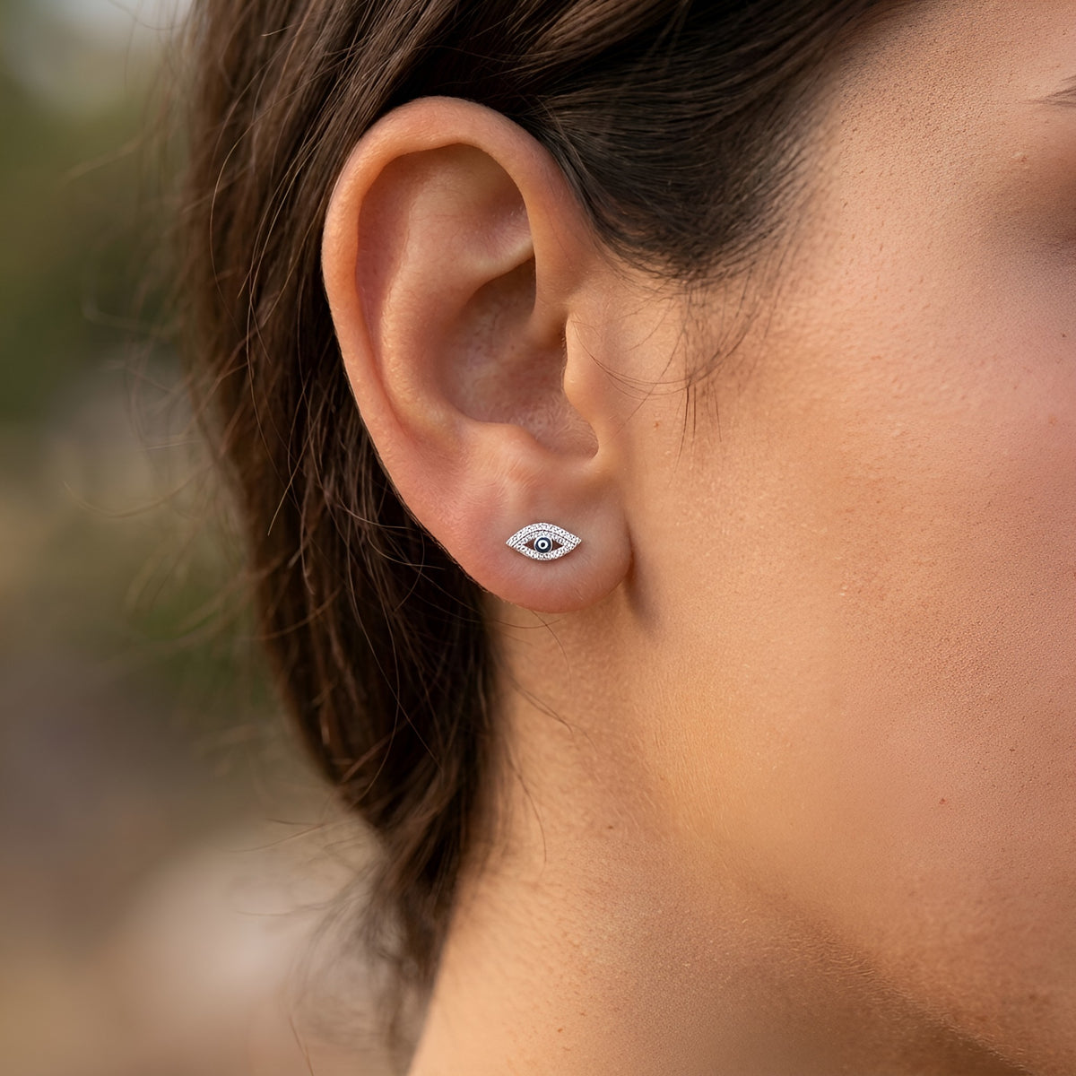 A close-up of a person's ear wearing a small white and dark blue evil eye stud earring.
