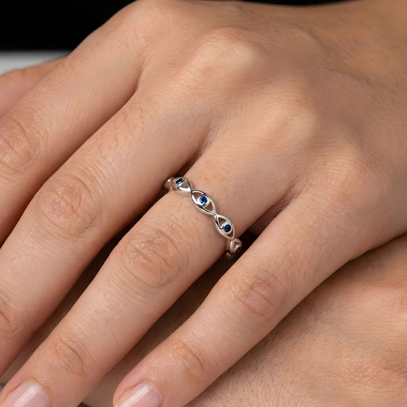 Silver evil eye ring with blue gemstones on a person's finger