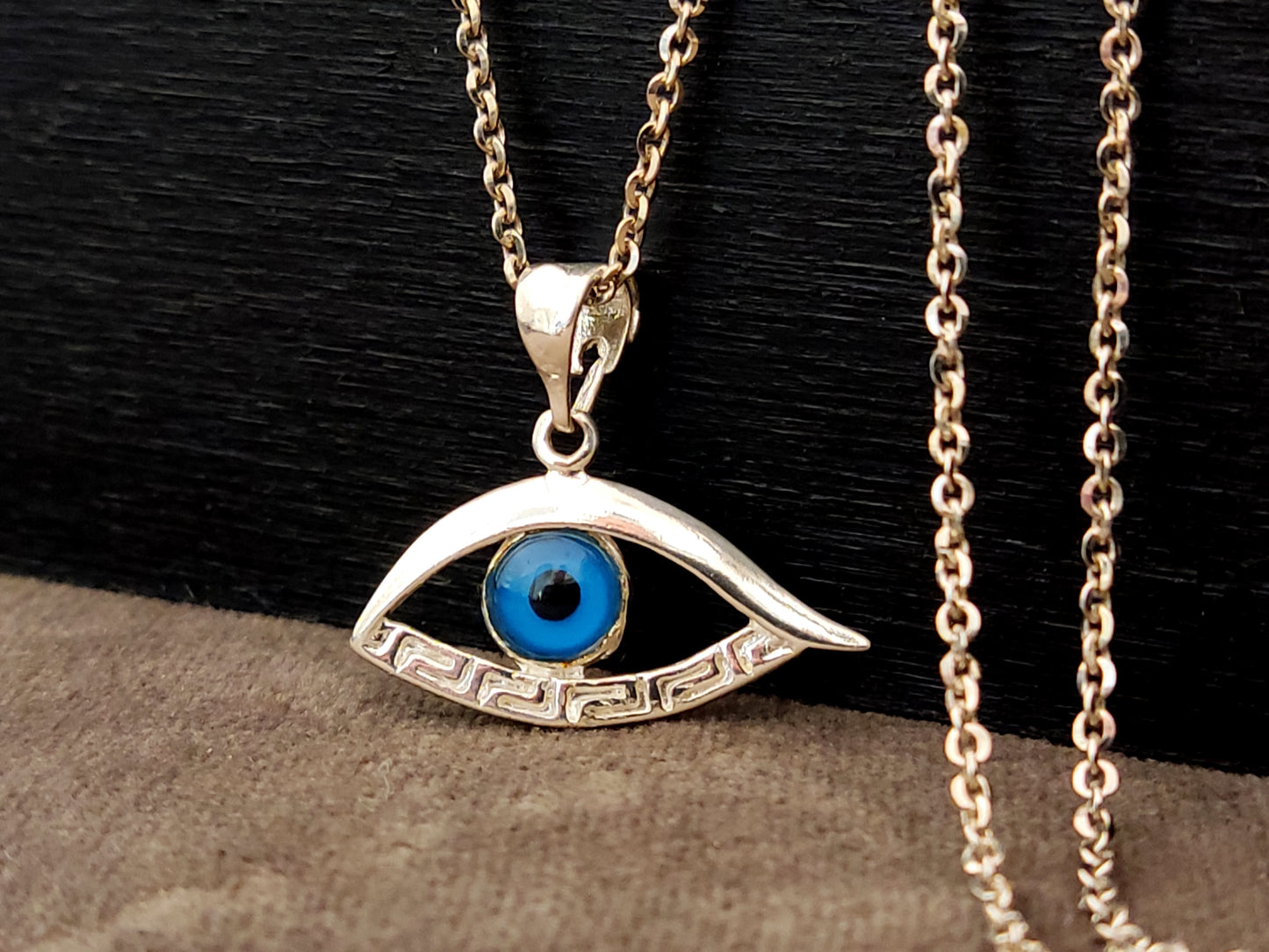 Evil eye shaped silver pendant with the Greek key on black and gray background.