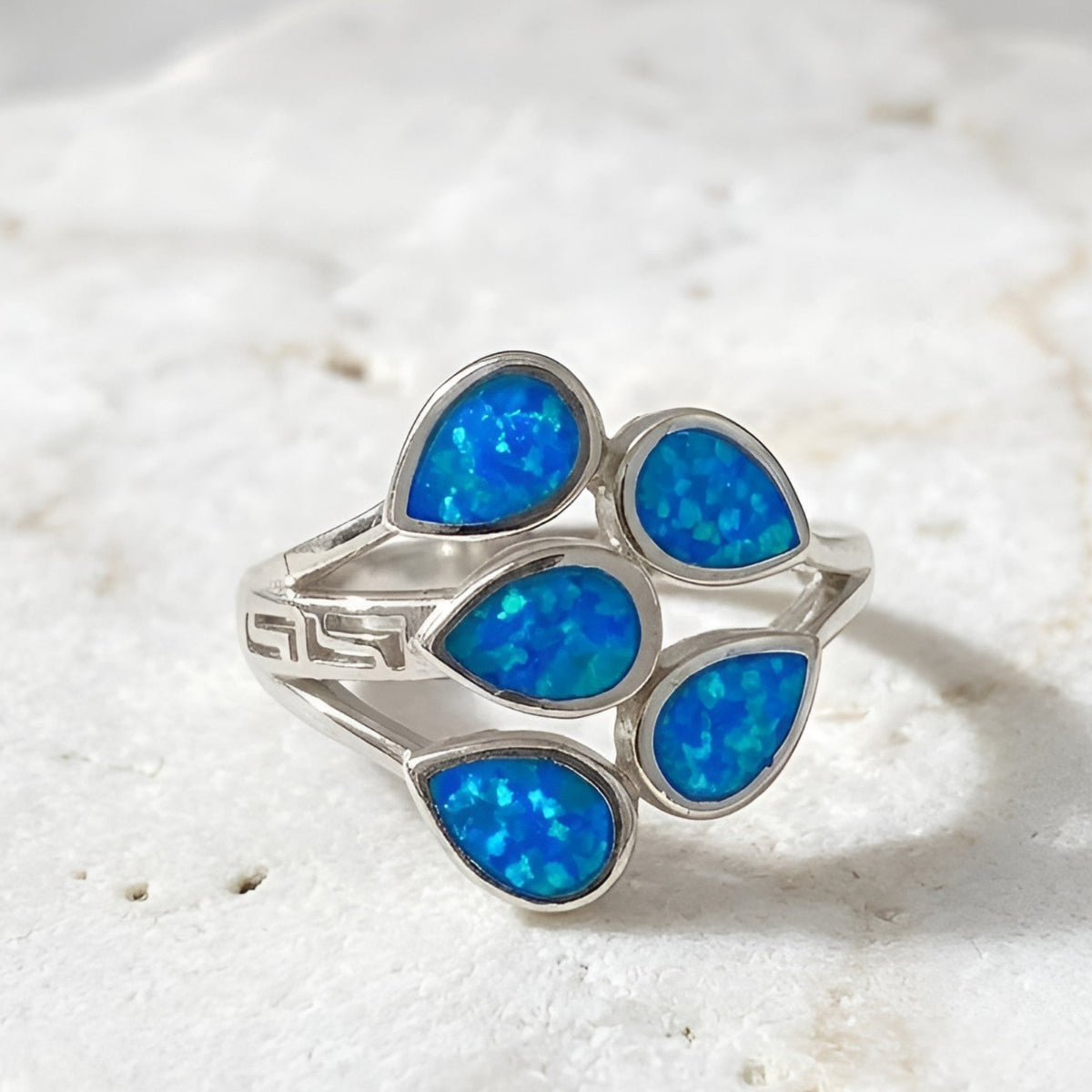 A Greek silver ring featuring five teardrop-shaped blue opal stones, displayed on a textured white stone surface.