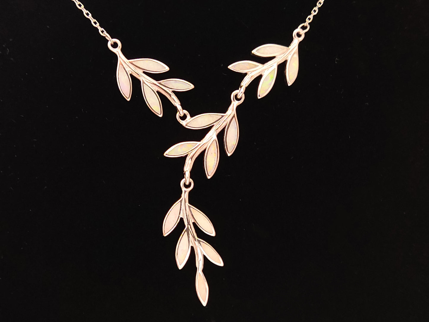 Greek silver necklace with leaves design and white opal stones on black background.
