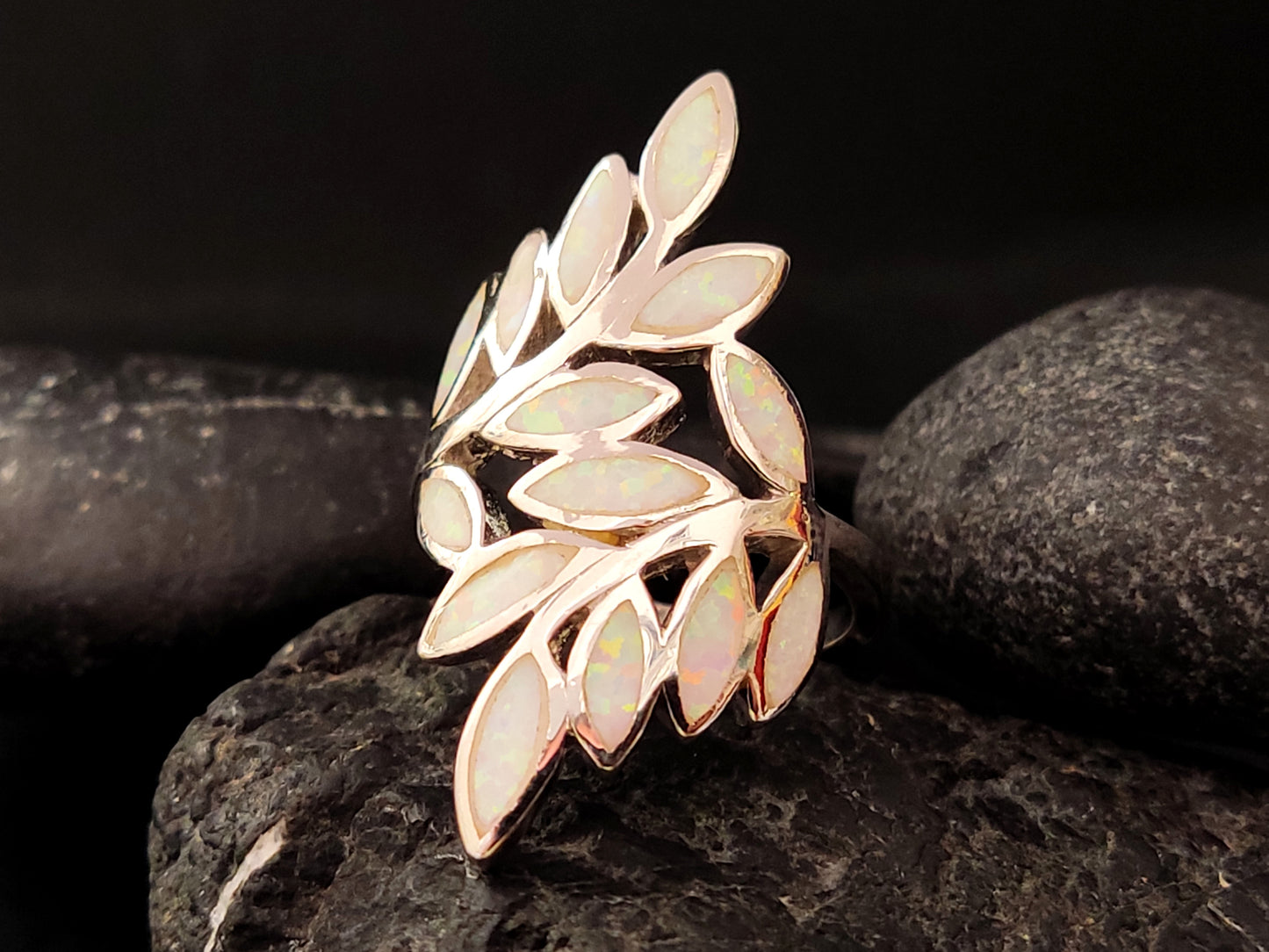 Greek silver ring with white opal leaves on black background.