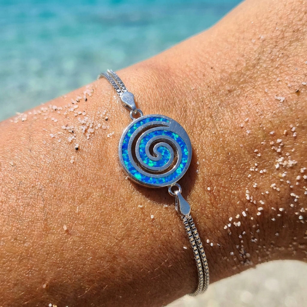 Silver bracelet with a blue spiral design on a wrist by the sea.