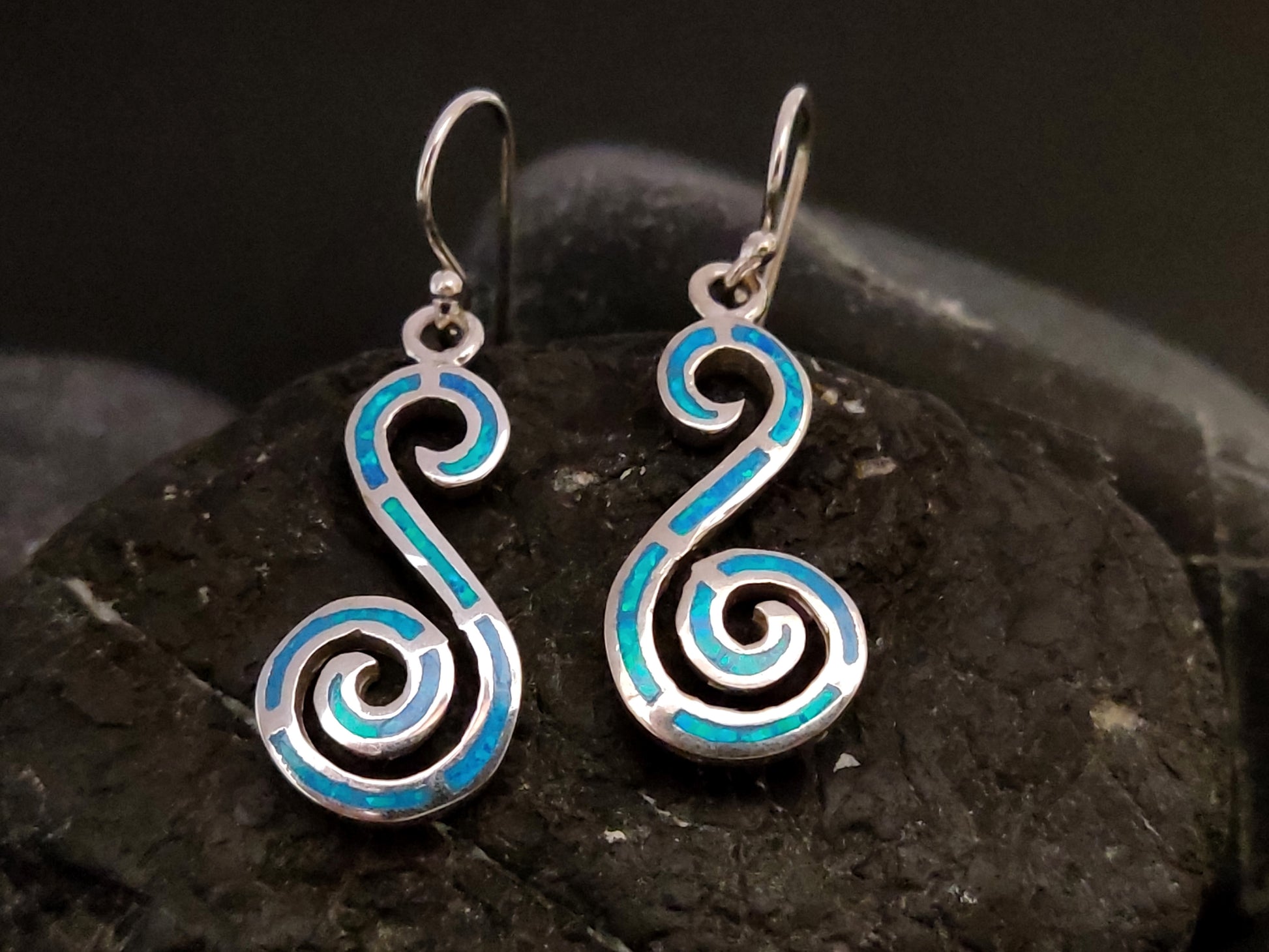 Blue opal double spiral dangle silver earrings on black rock.