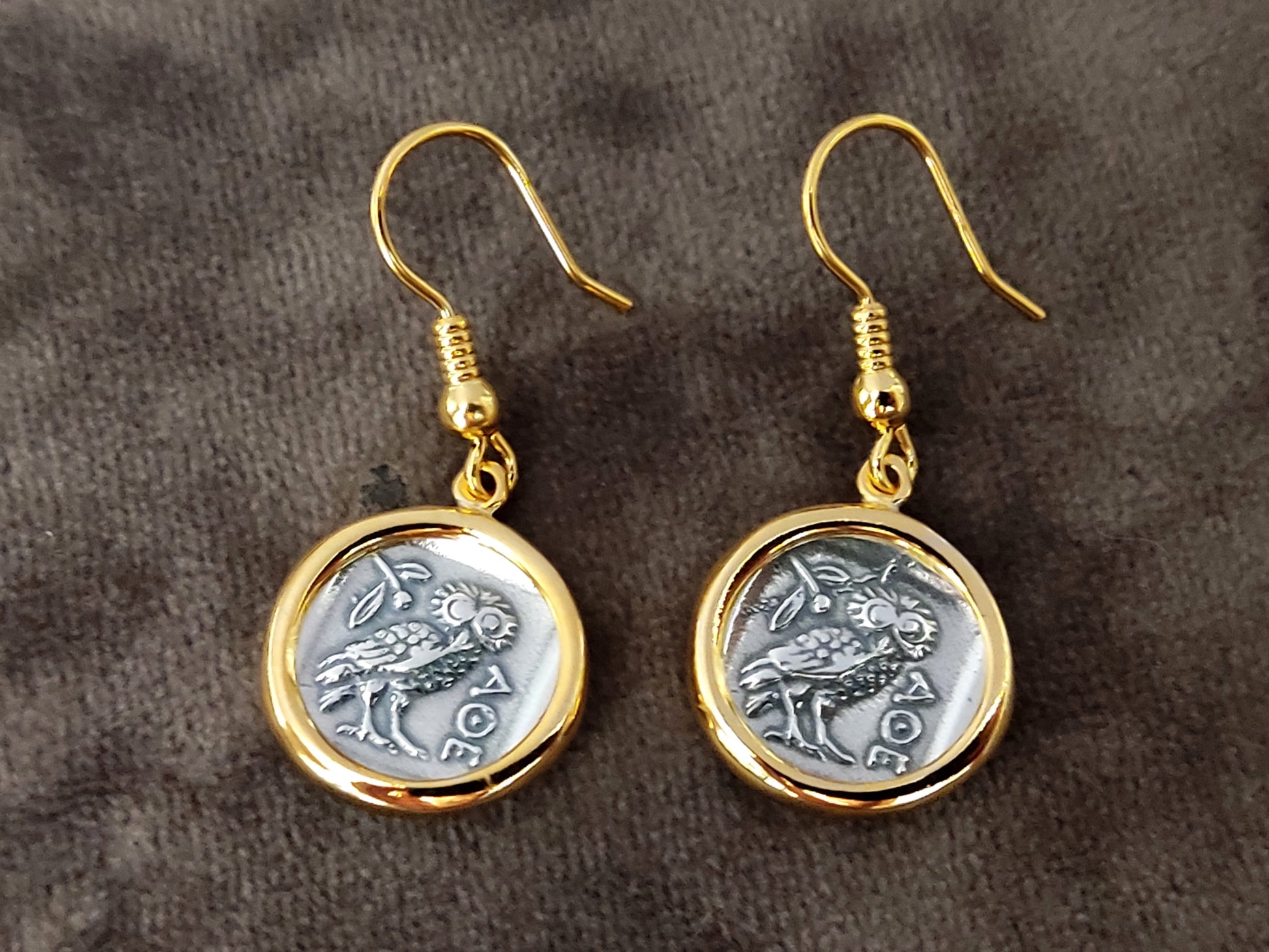 Greek silver earrings with the owl and goddess Athena on gray velvet.