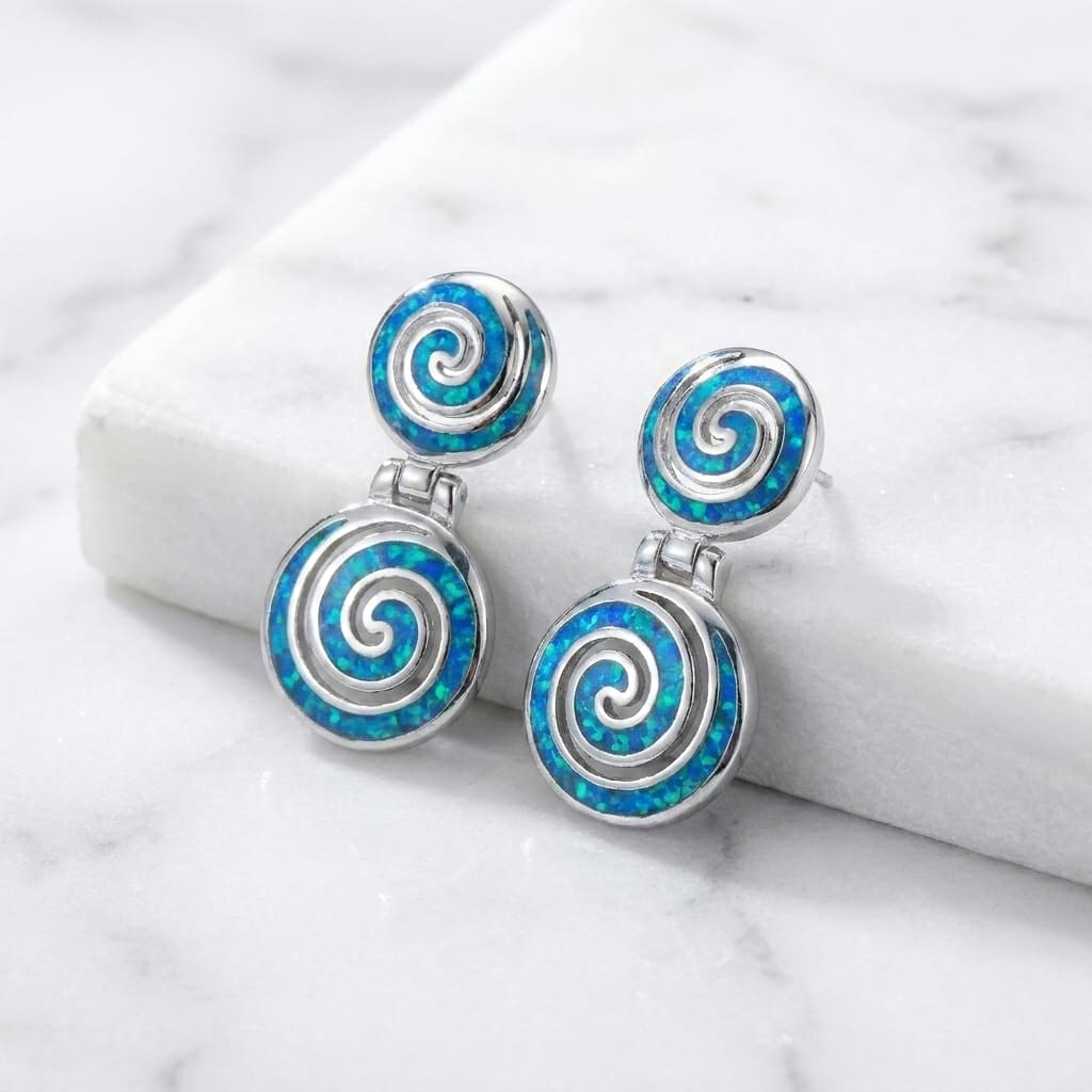 Pair of spiral earrings with blue and silver design on a white marble surface