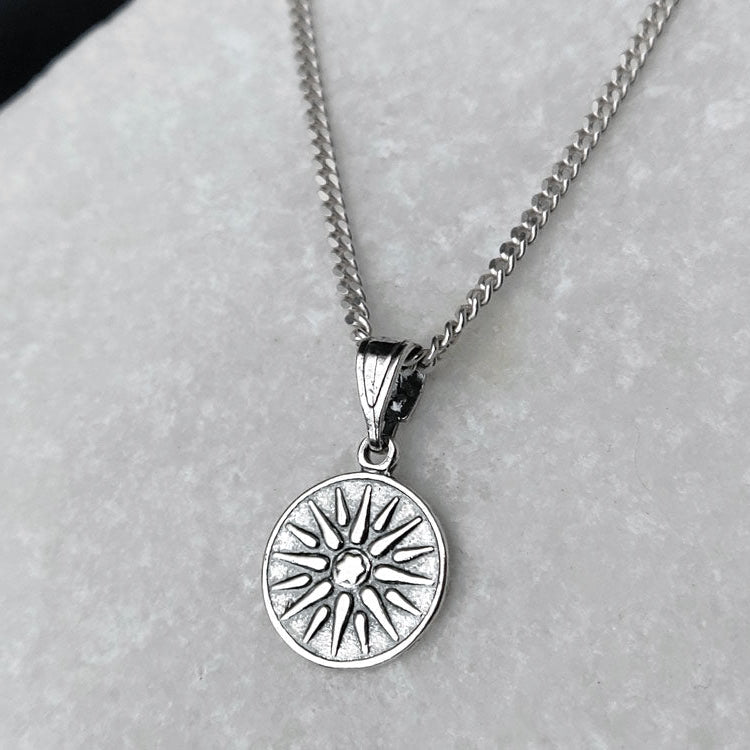 Silver necklace with a sun-shaped pendant on a light gray background