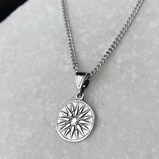Silver necklace with a sun-shaped pendant on a light gray background