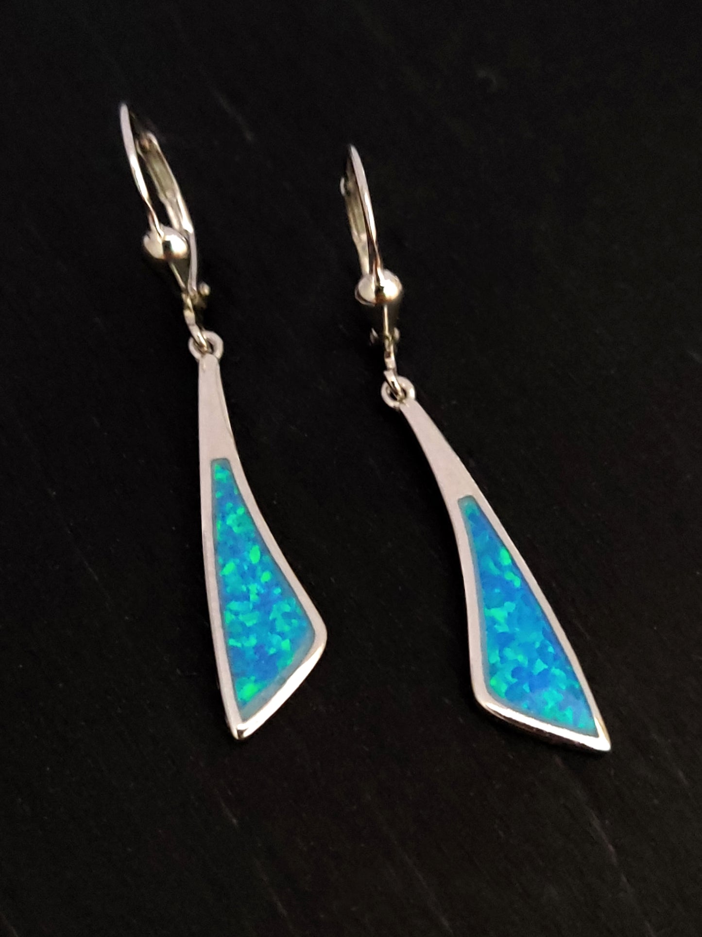 Dangle curved form earrings made of sterling silver 925 and blue opal stones on black background.