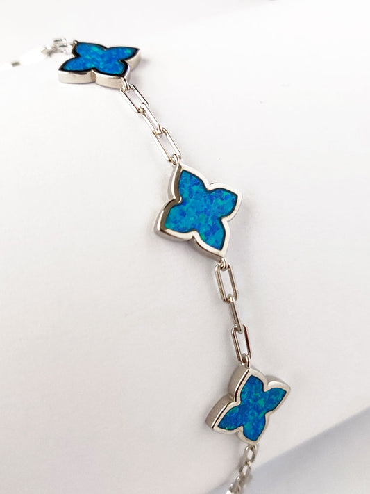 Sterling silver 925 bracelet made with 5 blue opal stones in cross shape. it has an adjustable length and made in Greece. The bracelet is laid on white background.