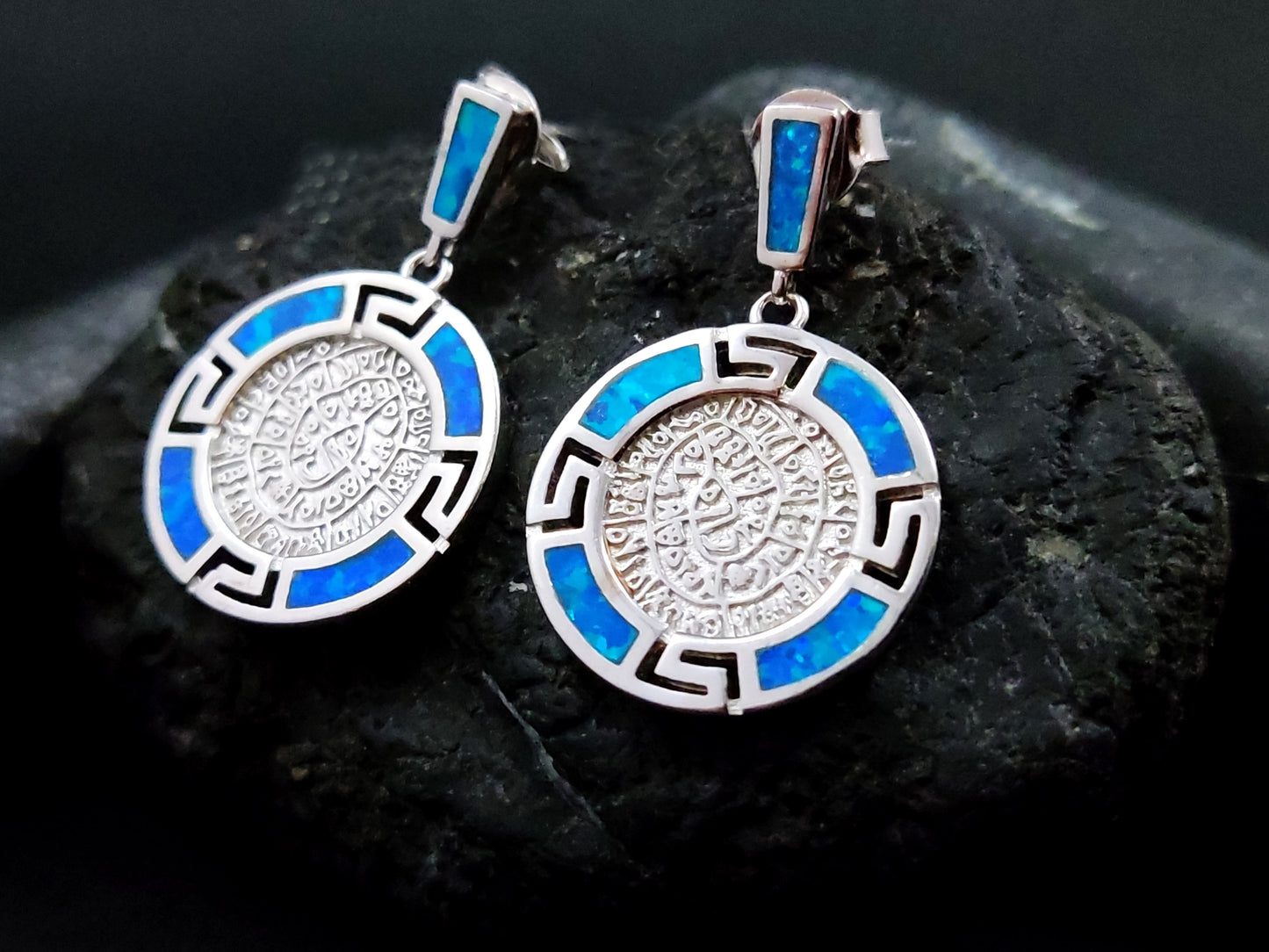 Phaistos Disc and Greek key design silver dangle blue opal earrings on black rock.