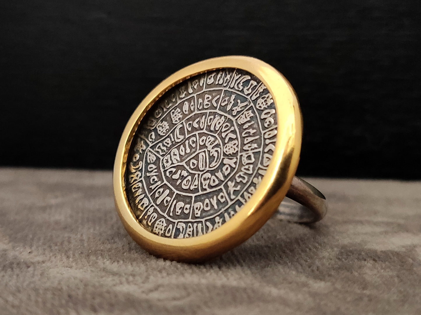 Phaistos Disc Greek silver ring with gold plated frame measuring 26mm on gray velvet and black backround.