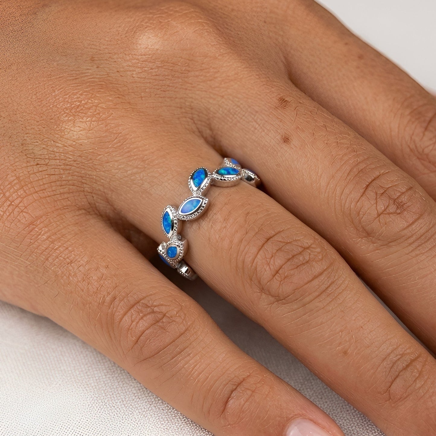 A close-up of a hand wearing a silver ring decorated with four marquise-cut blue opal stones set in a row.
