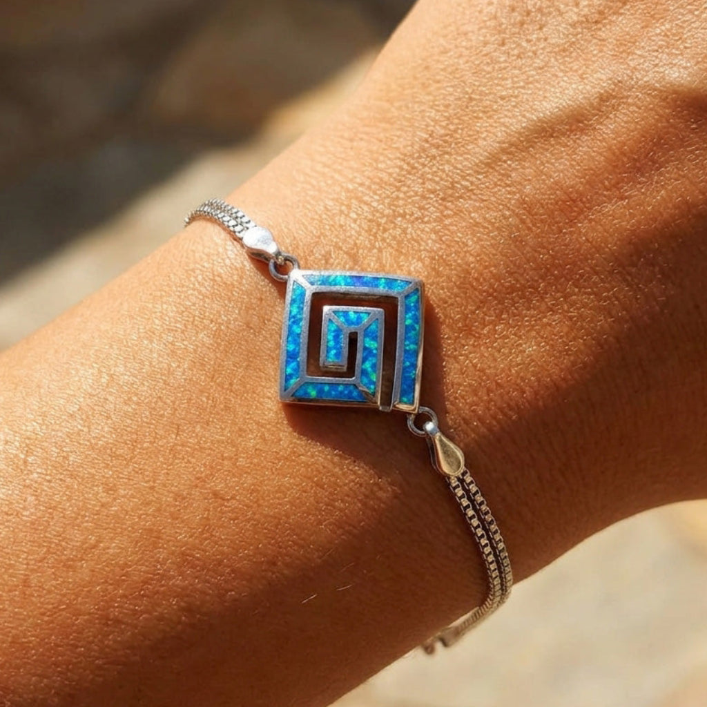 Close-up of a wrist wearing a blue square Greek Key blue opal design bracelet with a blurred natural background