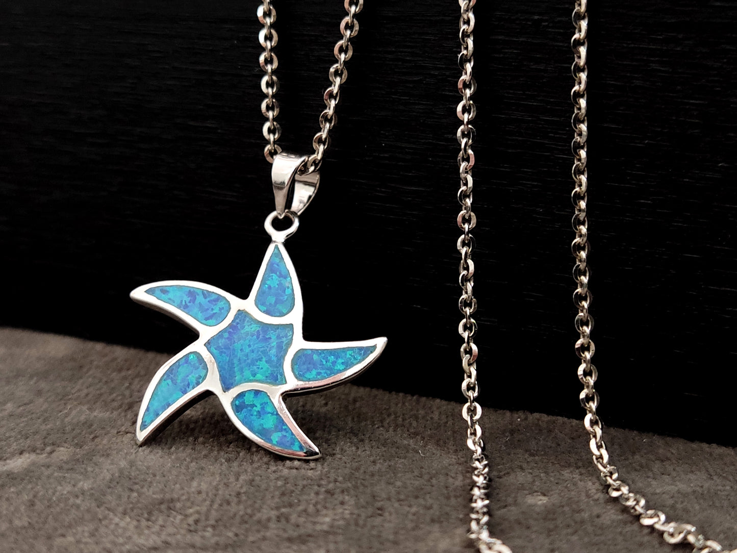 Starfish blue opal silver pendant measuring 25mm with silver fine chain on black and gray background.