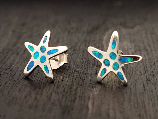 Starfish silver stud earrings with blue opal stones measuring 12mm on black background.