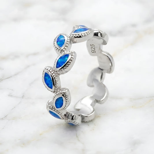 A sterling silver band ring featuring a series of marquise-cut blue opal inlays, photographed on a white marble surface. The inside of the band is stamped with '925' indicating sterling silver.