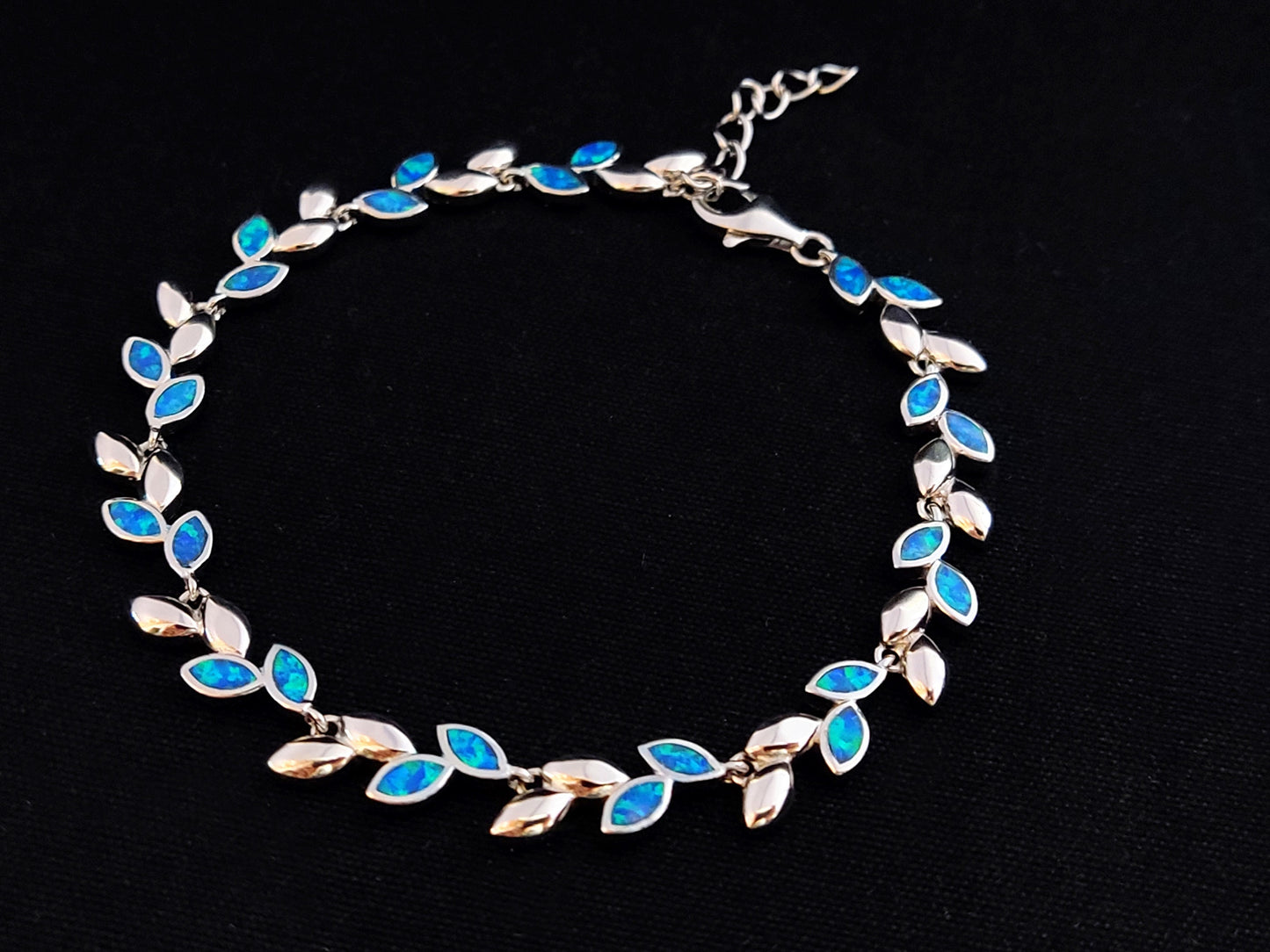 A sterling silver bracelet with Greek olive leaf design featuring blue opal stones on a black background.
