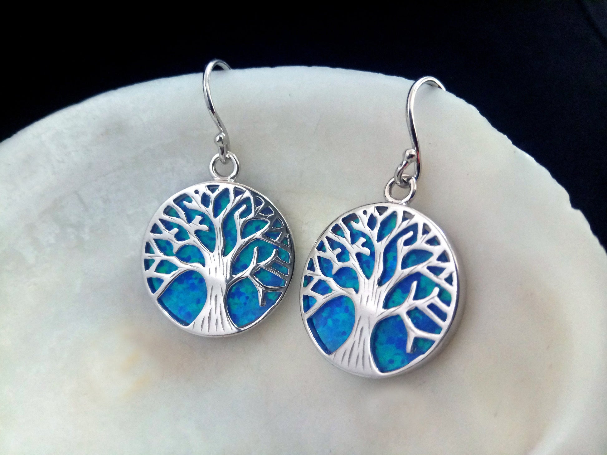 Silver earrings with the Tree Of Life design with blue opal stones on white shell background.