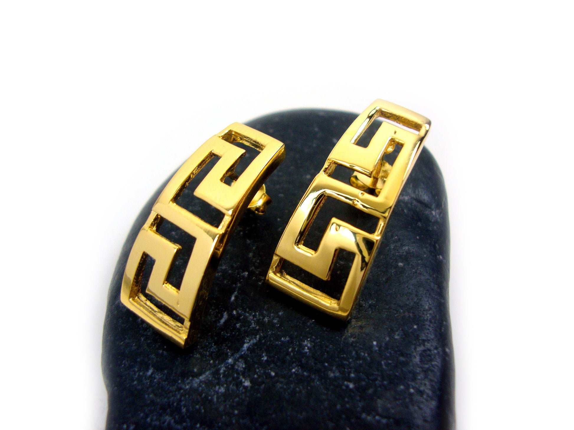 Greek key gold plated earrings on a black rock.