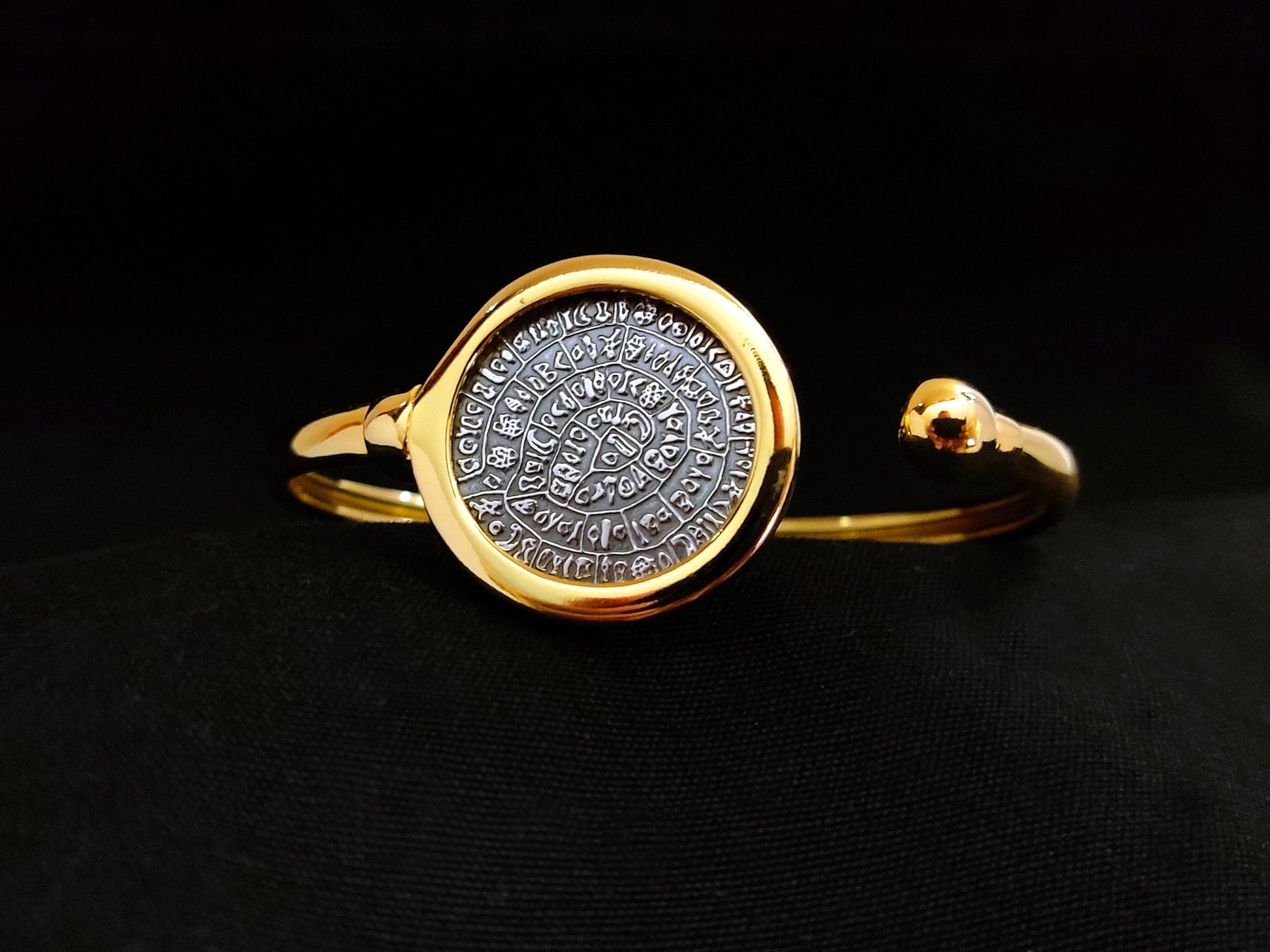 Close-up view of a Phaistos Disc silver Greek cuff bracelet with gold plating finish on black velvet.