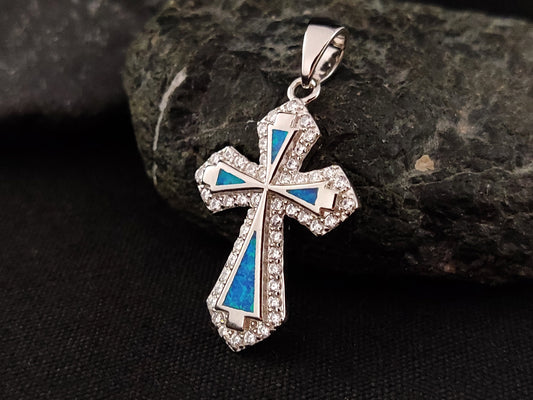 A sterling silver 925 cross made with blue opal stones and white crystals on black background.